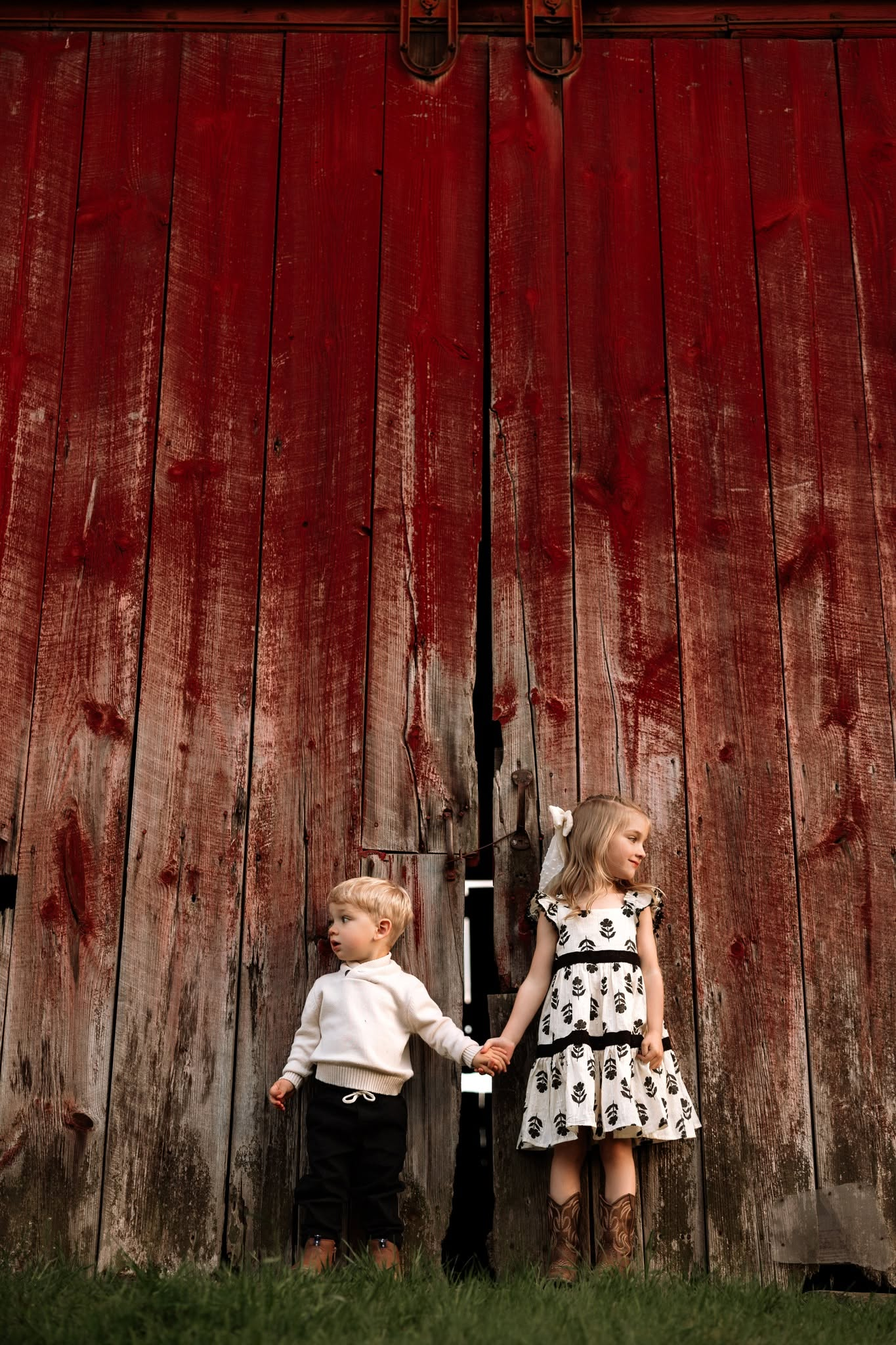 Siblings holding hands by a red barn door